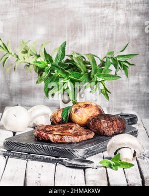 Auswahl an mittelseltenen Steaks, geschnitten mit Messer mit Kartoffelkeilen als Beilage. Kochen im Freien, und tolle Schnitte von Sirloin, Filet. Grill Stockfoto