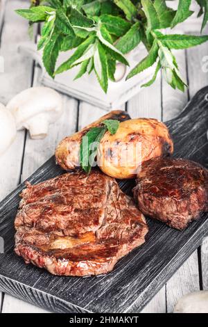 Auswahl an mittelseltenen Steaks, geschnitten mit Messer mit Kartoffelkeilen als Beilage. Kochen im Freien, und tolle Schnitte von Sirloin, Filet. Grill Stockfoto