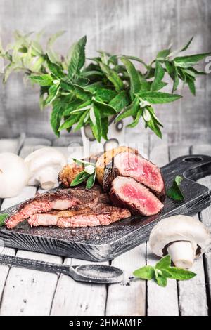 Auswahl an mittelseltenen Steaks, geschnitten mit Messer mit Kartoffelkeilen als Beilage. Kochen im Freien, und tolle Schnitte von Sirloin, Filet. Grill Stockfoto