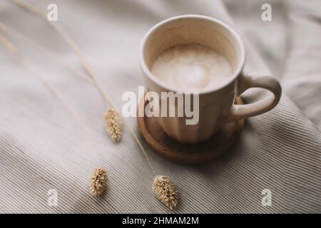 Tasse Kaffee mit Milch auf beigefarbenem Textil. „Still Life“-Frühstückskonzept. Warme und komfortable Atmosphäre Foto in hellen Pastellfarben. Stockfoto