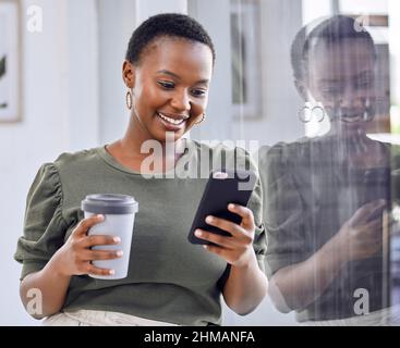 Eine kurze Pause einlegen, bevor Sie wieder in die Arbeit gehen. Aufnahme einer Geschäftsfrau, die Kaffee trinkt und ihr Mobiltelefon benutzt, während sie im Büro steht. Stockfoto