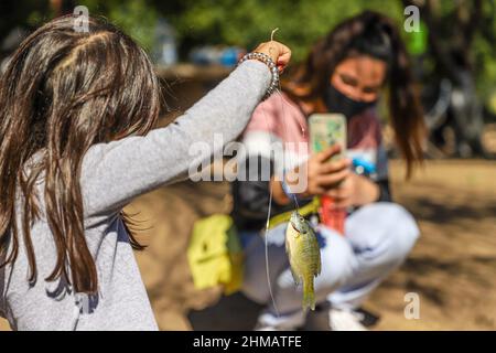 Una Niña observa un pez lobina de la pesca deportiva y recreativa que practican las familias hermosillenses en el humedal del Parque La Sauceda, su madre le Toma una fotografia con su telefono inteligente, Ein Mädchen beobachtet einen Barschfisch aus dem Sport- und Freizeitfischen, das Familien aus Hermosillo im Feuchtgebiet des La Sauceda Parks praktizieren, ihre Mutter fotografiert ihn mit ihrem Smartphone, Am 5. Februar 2022 in Hermosillo, Mexiko, anlässlich des Welttages der Feuchtgebiete zur Förderung der Erhaltung und Erhaltung der biologischen Vielfalt der Ökosysteme. (Foto von Luis Gutierrez Norte Photo/) Stockfoto