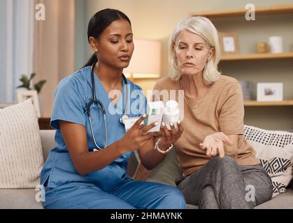 Bleiben Sie zu Hause und lassen Sie sich gut versorgen. Aufnahme eines Arztes, der während einer Konsultation mit einer älteren Frau zu Hause über Medikamentenoptionen diskutiert. Stockfoto