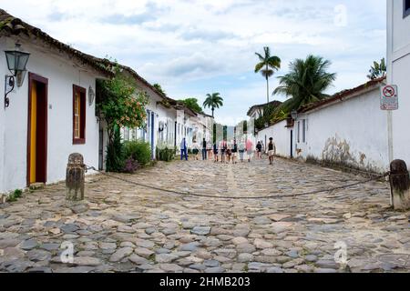 Touristen, die in den Kopfsteinpflasterstraßen im portugiesischen Kolonialstil spazieren. Alte Gebäude aus der gleichen Zeit sind auf beiden Seiten zu sehen. Stockfoto