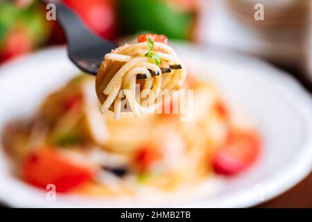 Frische Pasta mit Spaghetti, Tomaten, Pilzen, Basilikum und Parmesankäse auf weißem Teller auf Holzboden mit Zutaten im Hintergrund Stockfoto