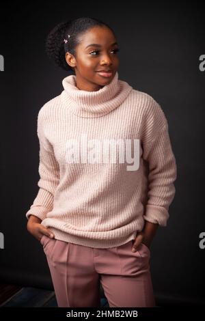 Eine coole junge schwarze Frau, die einen Rollkragenpullover mit ihren Händen in den Taschen trägt Stockfoto