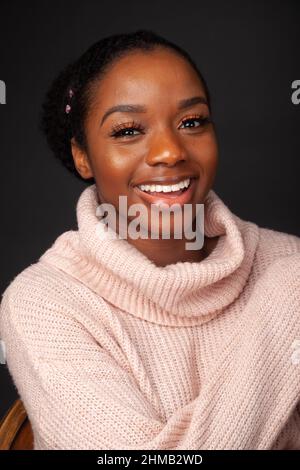 Ein Porträt einer schönen jungen schwarzen Frau, die lacht und einen Rollkragenpullover trägt. Stockfoto