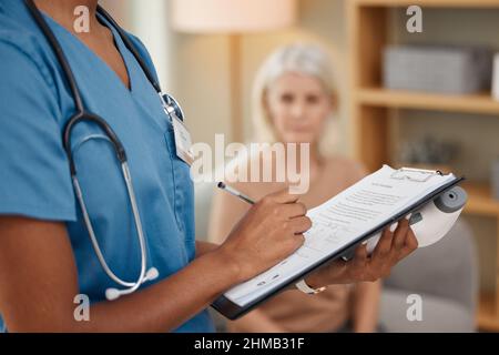 Dieser Arzt macht Hauslieferungen. Aufnahme eines Arztes, der während einer Konsultation mit einer älteren Frau zu Hause einen Fragebogen ausfüllt. Stockfoto