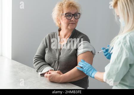 Allgemeinmediziner impft alten Patienten in der Klinik mit Kopierplatz. Arzt, der einer älteren Frau im Krankenhaus eine Injektion verabreicht. Krankenschwester hält Spritze Stockfoto
