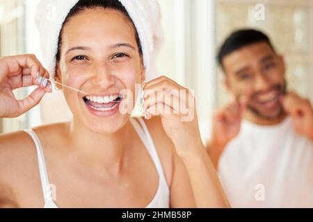 Zahnseide, damit Sie Ihr Lächeln mit Zuversicht zeigen können. Aufnahme eines glücklichen jungen Paares, das im Badezimmer zu Hause die Zähne mit Zahnseide putzt. Stockfoto