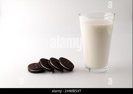 Eine Reihe von Schokoladencremesklätzchen neben einem Glas voller Milch auf einem isolierten weißen Hintergrund. Stockfoto