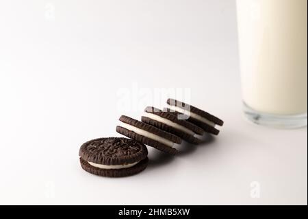Nahaufnahme einer Reihe von Schokoladencremesussen neben einem Glas voller Milch auf einem isolierten weißen Hintergrund. Stockfoto