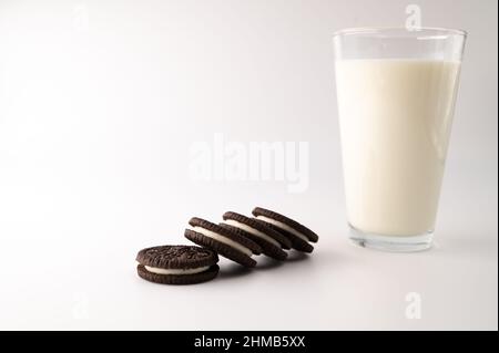 Milch in einem Glas mit einer Reihe Schokoladencremesueks daneben auf einem isolierten weißen Hintergrund. Stockfoto