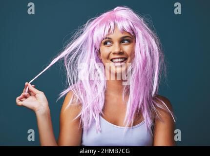 Wohin Sie auch gehen, nehmen Sie Ihren eigenen Sonnenschein mit. Studioaufnahme einer schönen jungen Frau, die mit einer verspielten rosa Perücke vor blauem Hintergrund posiert. Stockfoto