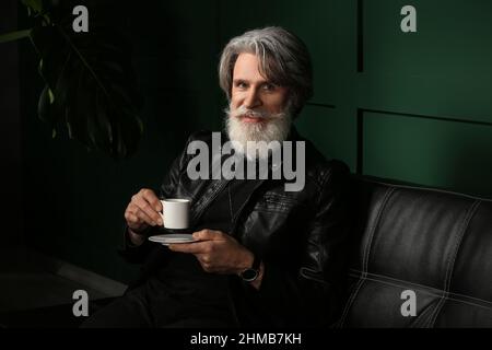 Hübscher reifer bärtiger Mann, der zu Hause Kaffee trinkt Stockfoto