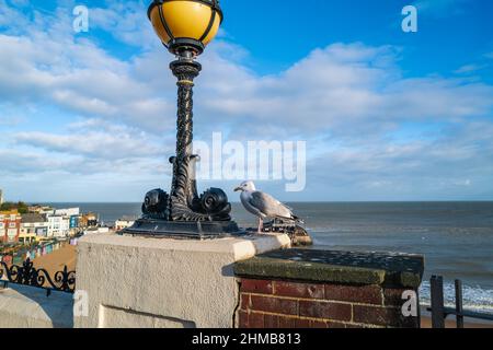 Eine Möwe hoch über der Viking Bay in Broadstairs, Kent, Großbritannien, neben einer verzierten Straßenlampe mit Fischen im Design. Stockfoto