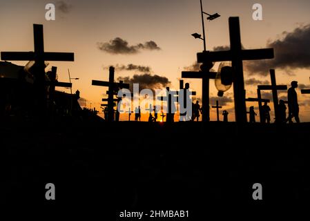 Silhouette von Menschen und Kreuzen, die auf dem Boden zu Ehren der von Covid-19 Getöteten befestigt sind. Sonnenuntergang in Salvador, Bahia, Brasilien. Stockfoto