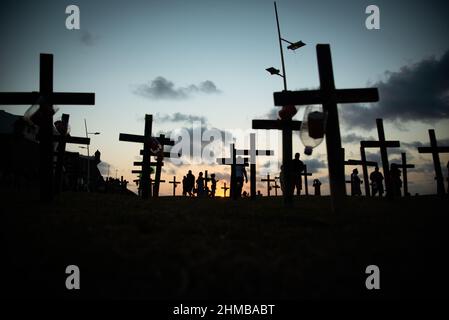 Silhouette von Menschen und Kreuzen, die auf dem Boden zu Ehren der von Covid-19 Getöteten befestigt sind. Sonnenuntergang in Salvador, Bahia, Brasilien. Stockfoto