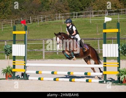 Mädchen und Pony springen über Hürde beim Springreiten Stockfoto