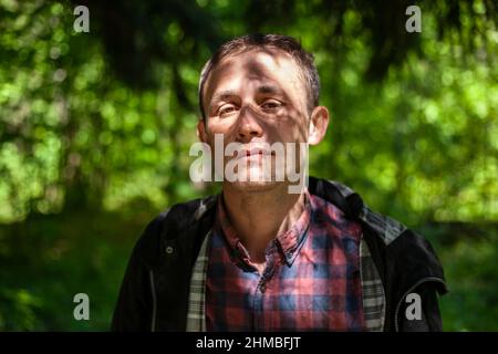 Porträt von Kerl in Wäldern. Mensch in der Natur. Das Gesicht wird durch Blätter schattiert. Der Mensch träumt davon. Brütenden Mann. Junger Europäer und Student. Mann im Park. Stockfoto