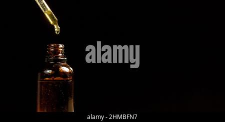 Cannabidiolöl in einer kleinen bernsteinfarbenen Flasche auf schwarzem Hintergrund, Nahaufnahme. Tropfendes CBD-Öl tropft mit einem Tropf. Stockfoto