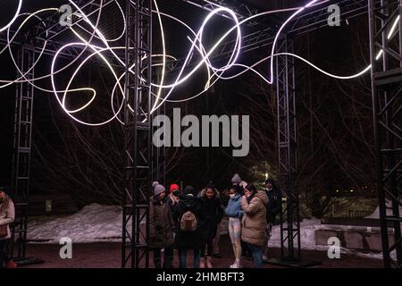 Toronto, Kanada. 07th. Februar 2022. Gemeinsam machen Menschen bei einer Außenkunstinstallation ‘Pressure' von Hans E. Madsen und Frederik D. Hougs ein Gruppenbild, ein Stück, das aus einer 300 Meter langen Kette pulsierender RGB-LED-Leuchten besteht, die einem Doodle ähneln und um eine große Konstruktion gewickelt sind. Die Nordic Lights Outdoor-Winterausstellung ist eine Ausstellung nordischer und kanadischer Lichtkunst im Toronto Harbourfront Centre, die gemeinsam mit Fjord Studio produziert wurde. (Foto von Katherine Cheng/SOPA Images/Sipa USA) Quelle: SIPA USA/Alamy Live News Stockfoto