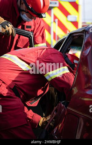 Ein Paar Ersthelfer arbeitet daran, einen Patienten, der bei einem Autounfall gefangen ist, zu befreien. Stockfoto