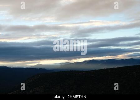 Himmel über hügeligen Berggipfeln. Lange Wolken filtern Sonnenlicht Stockfoto