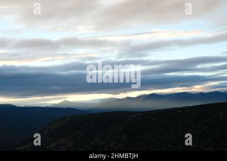 Himmel über hügeligen Berggipfeln. Lange Wolken filtern Sonnenlicht Stockfoto