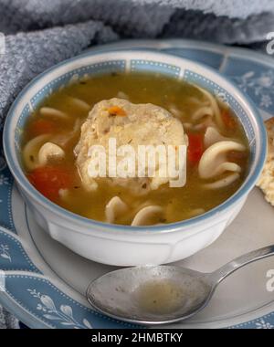 Eine perfekte Matzo-Kugel sitzt in einer heißen, herzhaften Schüssel mit Hühnersuppe mit Nudeln und Karotten, Sellerie und Huhn Stockfoto