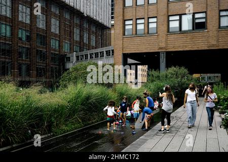Eine Gruppe von Kindern mit ihren Betreuern, Lehrer, die im Wasser auf der High Line spielen, dem beliebten Stadtpark von New York auf einer stillgewordenen Eisenbahnbrücke; heißer Sommertag. Stockfoto