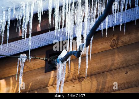 Eiszapfen hängen im Frühjahr bei Sonnenstrahlen vom Dach und von elektrischen Drähten. Gefährliche Wetterbedingungen Stockfoto