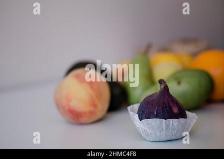 Frische Feige im Vordergrund mit anderen Früchten auf hellem Hintergrund auf dem Tisch Stockfoto