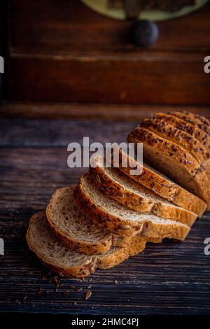 Frisch gebackenes Vollkornflachs- und Sonnenblumenkerebrot auf rustikalem Holztisch mit Brotkasten und Kopierraum geschnitten. Vertikale Ausrichtung. Stockfoto