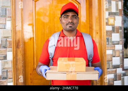 Delivery boy mit Pappkartons Blick auf die Kamera vor der Tür - Konzept des kleinen Unternehmens, Kurierdienst und schnelle Lieferung Stockfoto