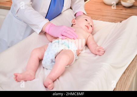 Der Arzt macht Gymnastik und massiert ein neugeborenes Baby. Krankenschwester in Uniform, die dem Kind Aufwärmübungen macht Stockfoto