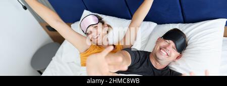 Junge Männer und Frauen, die Schlafmasken tragen und ihre Hände im Bett strecken Stockfoto