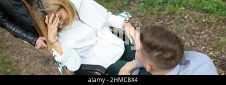 Junge behinderte Frau im Rollstuhl weint in der Nähe eines Mannes, der vor ihr im Park sitzt Stockfoto