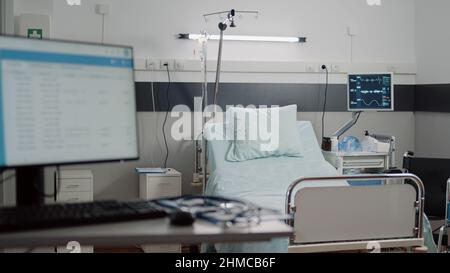 Leeres Bett auf der Krankenhausstation mit medizinischen Geräten für die Gesundheitsversorgung und Erholung. Niemand im Reanimationsraum mit Herzfrequenzsensor und Infusionsbeutel für Intensivpflege und Hilfe. Stockfoto