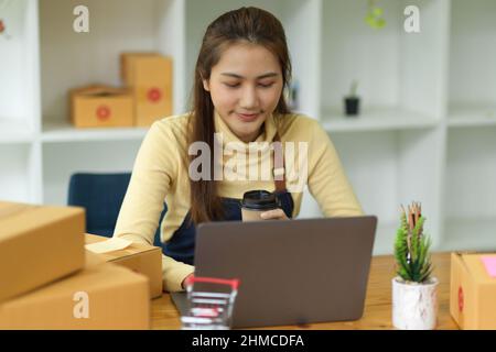 Schöne asiatische junge weibliche Online-Shopping-Business-Besitzer arbeitet auf Laptop-Computer mit Paketkasten in ihrem Home Office. Online-Verkauf, KMU busines Stockfoto
