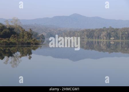 Frischer Morgen mit nebligen Himmel und Blick auf die Berge und Waldreflexe auf dem Seewasser Stockfoto