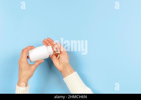 Bunte Medikamente Pillen und Kapseln in der Hand der Frau auf pastellblauem Hintergrund. Weibliche Hand verschütten Pillen aus der weißen Flasche Apotheke, Medizin und Stockfoto