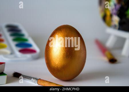 Goldenes Osterei auf einem Aquarell-Hintergrund. Einfache Urlaubsgestaltung. Symbolik des Ostereier-Festes. Kunstwerke, handgefertigt, Kreativität Stockfoto