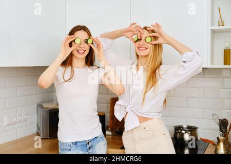 Zwei verspielte Frauen legen Gurken in die Augen, haben Spaß in der Küche Stockfoto