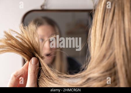 Junge Frau vor dem Spiegel traurig aufgeregt mit Haarausfall Schaden Problem Stockfoto