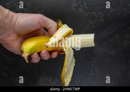 studioaufnahme einer Hand, die geschälte und halb gefressene Banane hält Stockfoto