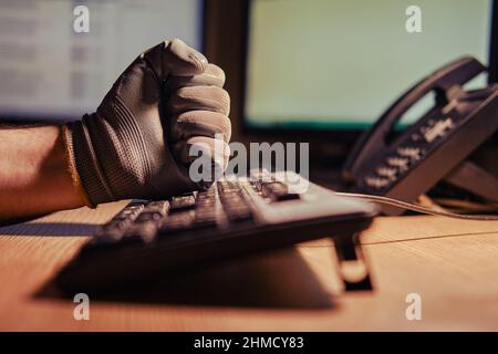 Mann hält sich in dunklen Handschuhen an, die vor dem Hintergrund eines Nachtbüros auf einer Computertastatur tippen Stockfoto