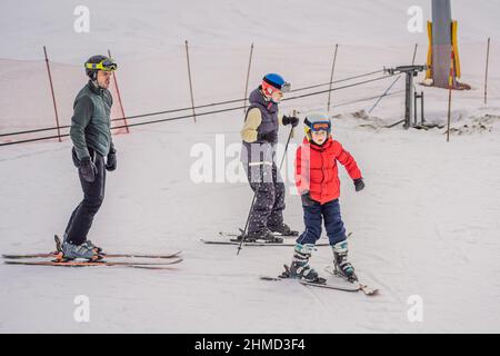 Mutter und Sohn lernen mit einem Lehrer Skifahren. Aktives Kleinkind mit Schutzhelm, Schutzbrille und Stöcken. Skirennen für kleine Kinder. Winter Stockfoto