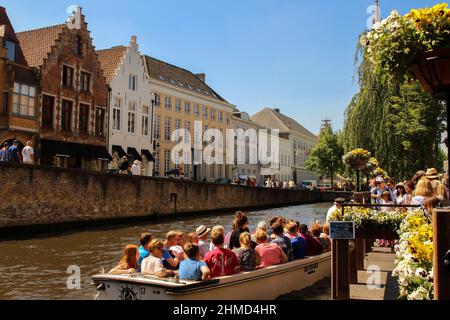 Ausflugsboot voller Touristen, das an einem sonnigen Sommertag auf dem Fluss durch Brügge, Belgien, andockt. Hochwertige Fotos. Stockfoto