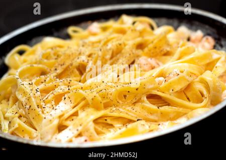 Tagliatelle Pasta mit Garnelen mit Sauce in der Pfanne. Italienische Gerichte werden zubereitet Stockfoto